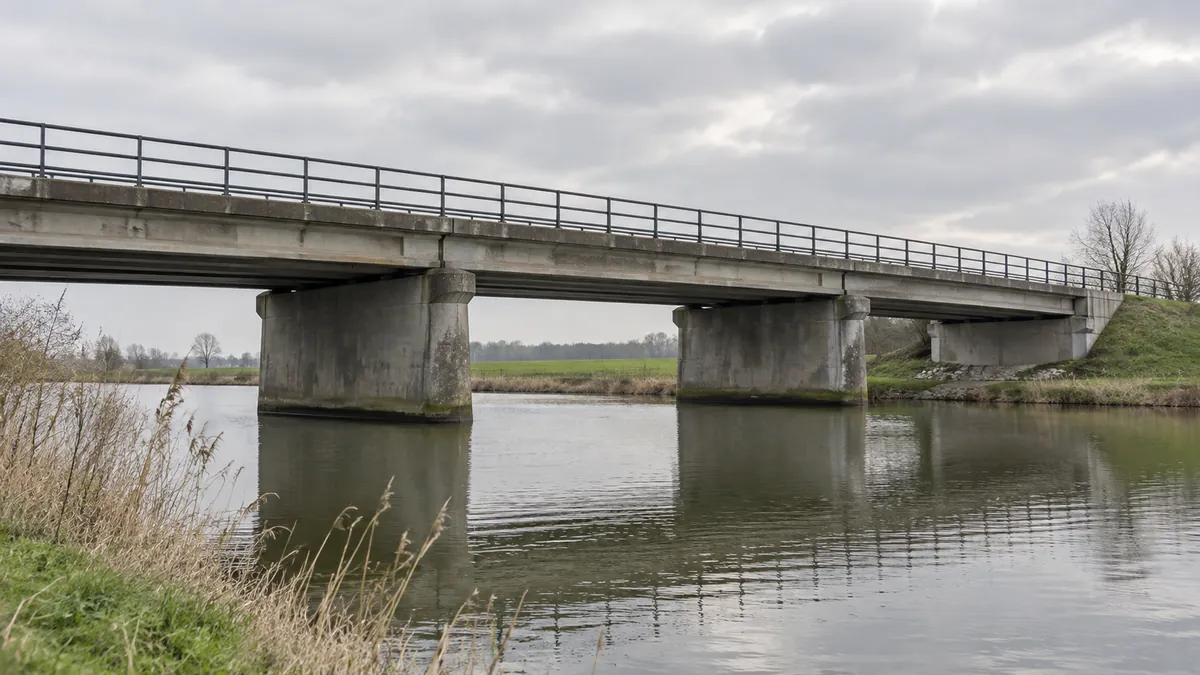 Een betonnen verkeersbrug over een rustig kanaal in een vlak landschap.